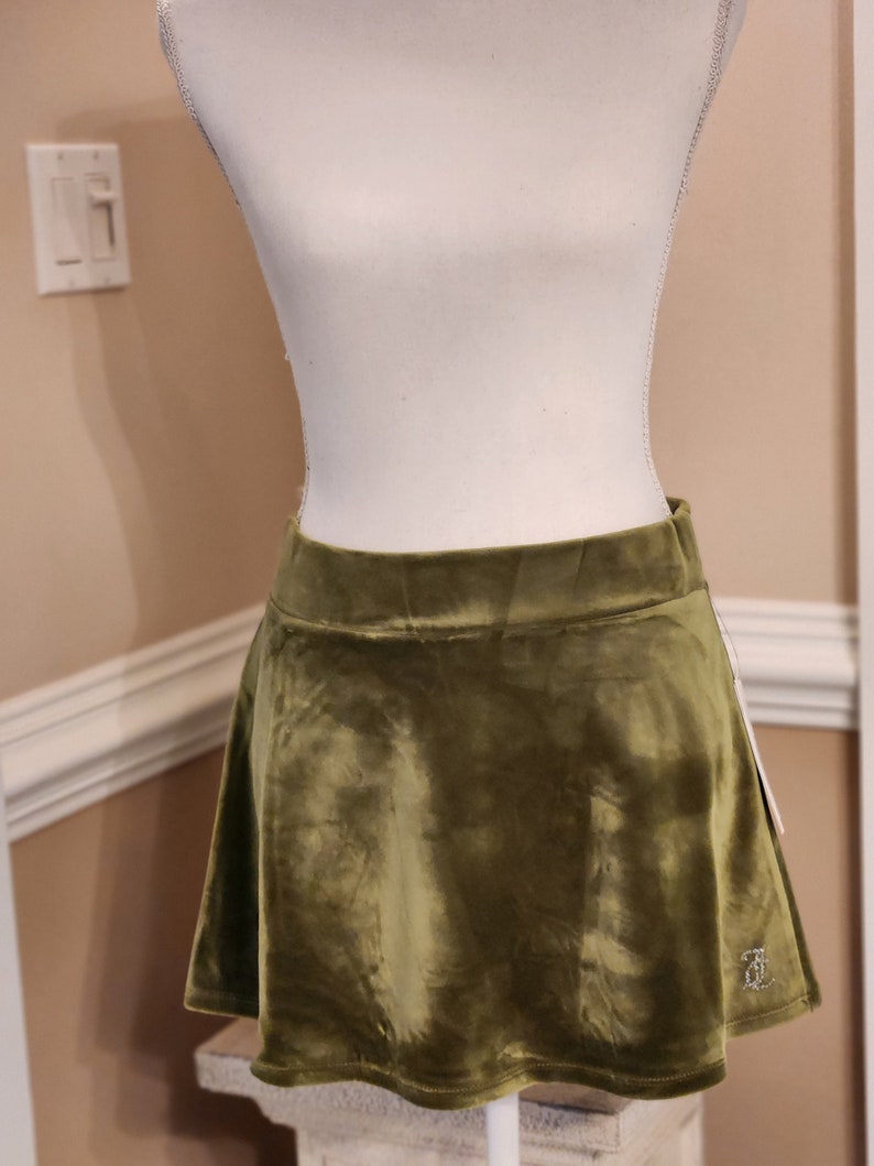 May include: A green velvet mini skirt with a flared hem. The skirt has a small embroidered logo on the bottom right side.