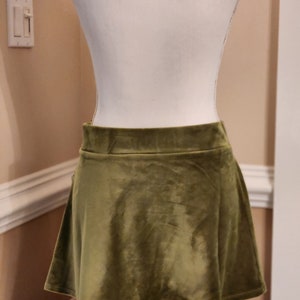 May include: A short, olive green velvet skirt with a flared hem.