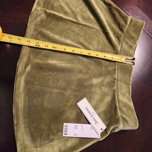 May include: A green velvet mini skirt with a Juicy Couture tag. The skirt has a small rhinestone logo on the front.