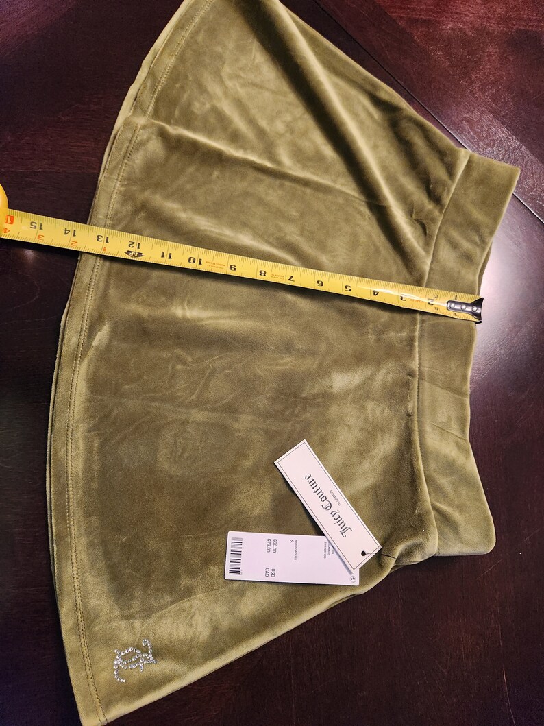 May include: A green velvet mini skirt with a Juicy Couture tag. The skirt has a small rhinestone logo on the front.