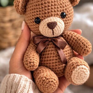 Può includere: Un orsacchiotto all'uncinetto fatto a mano nei toni del marrone e del beige. L'orso ha occhi di sicurezza neri, un muso marrone chiaro e un fiocco marrone scuro. Misura circa 15 cm di altezza.