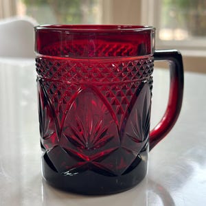 May include: A red glass mug with a cut glass design. The mug has a handle and is perfect for serving beverages.