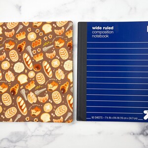 May include: Two composition notebooks. One has a brown cover with a pattern of pastries and cats. The other has a blue cover with the text "wide ruled composition notebook" and "90 sheets - 7 1/2 in x 9 1/4 in (19 cm x 24.7 cm)".