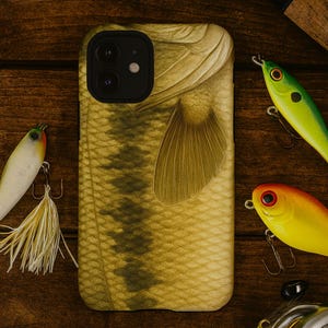 May include: A phone case featuring a detailed fish scale and fin design in shades of tan and olive green. Fishing lures in yellow, green, and orange are arranged around the phone case on a wooden surface.