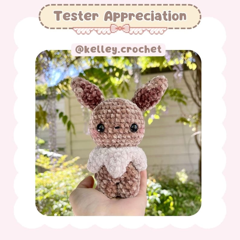 May include: A brown and pink crocheted Eeveelution plush toy with black eyes. The toy is being held in a person's hand.