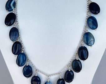May include: A silver chain necklace with multiple dangling oval-shaped blue agate stones. The stones have a marbled pattern with shades of blue.