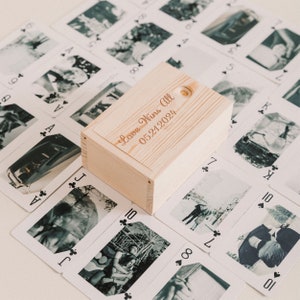 May include: A wooden box with the text "Love Wins All 05.21.2024" engraved on the top. The box is surrounded by playing cards with black and white photos.