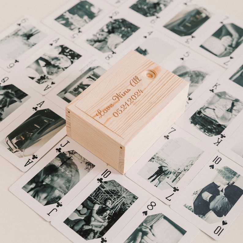 May include: A wooden box with the text "Love Wins All 05.21.2024" engraved on the top. The box is surrounded by playing cards with black and white photos.