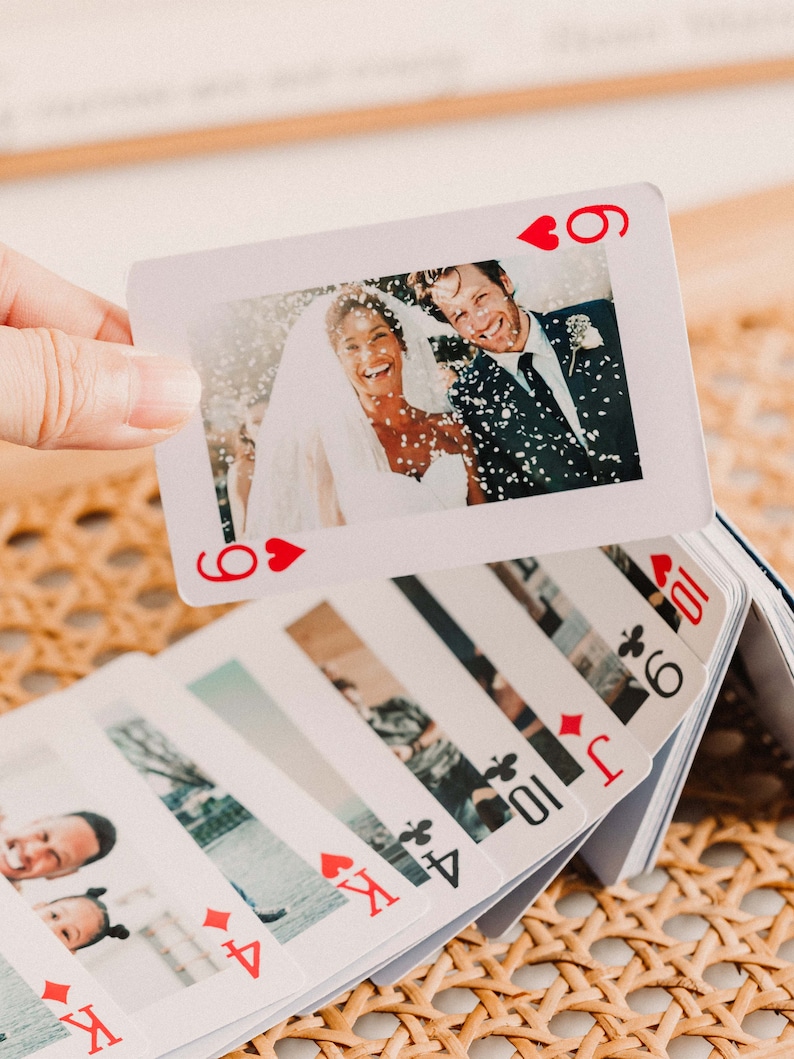 May include: A deck of playing cards with personalized photos on each card. The top card shows a wedding photo of a couple with confetti falling on them. The card is a 6 of hearts.
