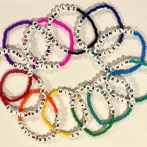 May include: A set of colorful beaded bracelets with the phrase "Mind Over Miles" repeated on each bracelet. The bracelets are made with small, colorful beads and feature white letters.