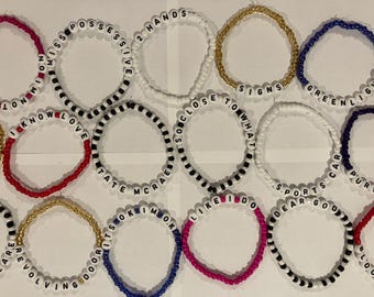 May include: A collection of colorful beaded bracelets with various words and phrases spelled out on them, including "I Know", "Love", "Possess", "Close To What", "Greenlight", "Sports", "Dear God", "Its So Kim Ok", "Like I Do", "Care", "Revolving", and "Purple".