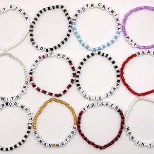 Puede incluir: Una colección de doce pulseras de cuentas con letras blancas que deletrean los títulos de canciones Dirty Diana, Smooth Criminal, PYT, Rock With You, King Of Pop, Billie Jean, Beat It, Black Or White, Human Nature, Thriller y Man In The Mirror.