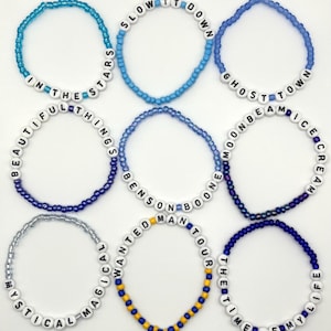 May include: Nine circular beaded bracelets featuring white letter beads spelling phrases including IN THE STARS, SLOW IT DOWN, GHOST TOWN, BEAUTIFUL THINGS, BENSON BOONE, MOONBEAM ICE CREAM, MYSTICAL MAGICAL, WANTED MAN TOUR, and THE TIME OF MY LIFE.