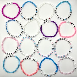 Puede incluir: Una colección de pulseras de cuentas de varios colores, cada una deletreando una frase o palabra diferente. Las pulseras presentan cuentas de letras blancas y cuentas de colores, incluyendo rosa, azul y morado. Las frases incluyen "LESS", "WHAT'S WRONG WITH ME" y "CIGARETTE SMOKE".