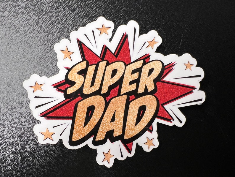 Op de afbeelding: Een rode en witte stripboek-stijl grafiek met gouden glitter accenten. De grafiek zegt "SUPER DAD" in vetgedrukte zwarte letters.