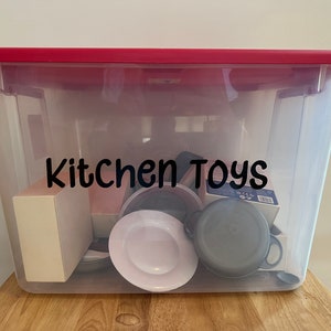 Pode incluir: Uma caixa de armazenamento de pl&aacute;stico transparente com uma tampa vermelha. A caixa est&aacute; cheia de v&aacute;rios brinquedos de cozinha, incluindo um prato branco, uma panela preta e uma caixa etiquetada como "Pieces 99". A caixa est&aacute; etiquetada como "Kitchen Toys" em letras pretas.