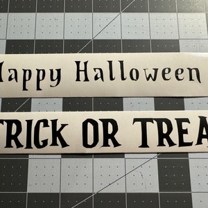 Pode incluir: Dois sinais brancos com texto preto. O sinal superior diz "Feliz Halloween" e o sinal inferior diz "Doces ou travessuras".