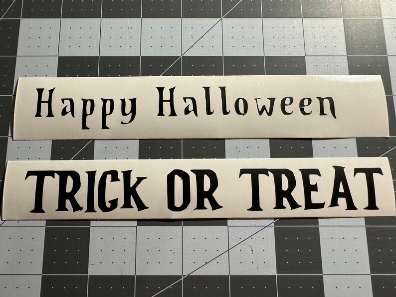 Pode incluir: Dois sinais brancos com texto preto. O sinal superior diz "Feliz Halloween" e o sinal inferior diz "Doces ou travessuras".
