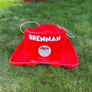 Pode incluir: Tren&oacute; de pl&aacute;stico vermelho com uma corda branca e o nome "BRENNAN" impresso na frente.