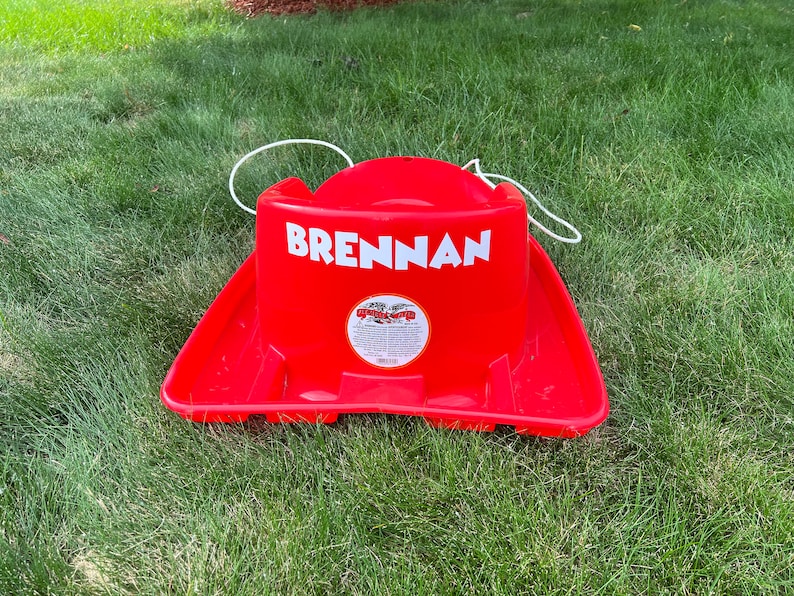 Pode incluir: Tren&oacute; de pl&aacute;stico vermelho com uma corda branca e o nome "BRENNAN" impresso na frente.