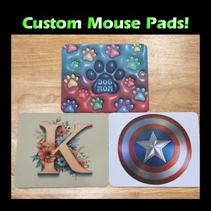 May include: Three custom mouse pads with different designs. The first mouse pad has a blue and pink background with paw prints and the text "Dog Mom". The second mouse pad has a beige background with a floral design and the letter "K". The third mouse pad has a white background with a red, white, and blue American flag design.