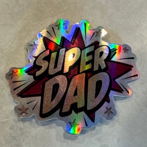 Op de afbeelding: Een zilveren holografische sticker met een rood stervormig ontwerp. De woorden "SUPER DAD" zijn in zwarte letters op de sticker gedrukt.