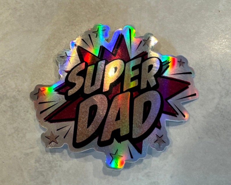 Op de afbeelding: Een zilveren holografische sticker met een rood stervormig ontwerp. De woorden "SUPER DAD" zijn in zwarte letters op de sticker gedrukt.