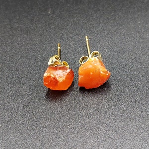 May include: A pair of orange carnelian earrings with gold settings. The carnelian is a rough, natural stone.