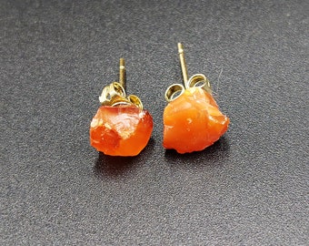 May include: A pair of orange carnelian earrings with gold settings. The carnelian is a rough, natural stone.