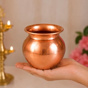 May include: A polished copper pot with a rounded body and a wide, flared rim. The metal surface is smooth and reflective, showcasing a warm, metallic orange-brown hue. The vessel features a simple, circular opening and a curved base design.