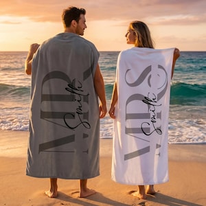 May include: A gray towel with the text MR Smith and a white towel with the text MRS Smith. Both towels feature large, bold, dark gray lettering and cursive script text printed vertically across the fabric, displayed as rectangular pieces of cloth.