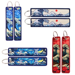 May include: Set of six keychains featuring different Japanese art prints. Two keychains feature a blue and white wave design, two feature a red and white wave design, and two feature a blue and white starry night design.