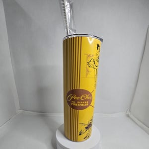 May include: A yellow and brown tumbler with a vintage illustration of a woman ice skating. The tumbler has the text "Pee-Chee All Season Portfolio" printed on it.