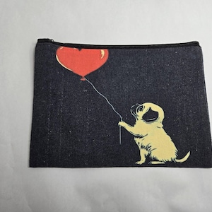 May include: A rectangular, black denim-textured pouch with a black zipper. The pouch features a cream-colored illustration of a pug holding a red heart-shaped balloon. The balloon is connected to the pug by a thin white string.