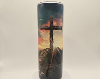 May include: A stainless steel tumbler with a colorful sunset scene and a wooden cross on a mountaintop.