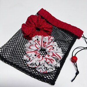 May include: A black mesh drawstring bag with a red and white polka dot trim. The bag contains two fabric scrunchies, one red with white polka dots and one white with red and black lettering.