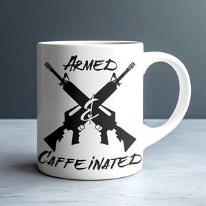 Pode incluir: Caneca de cerâmica branca com um gráfico preto de dois rifles cruzados e as palavras "ARMED & CAFFEINATED". A caneca tem uma alça curva e está sobre um fundo neutro.