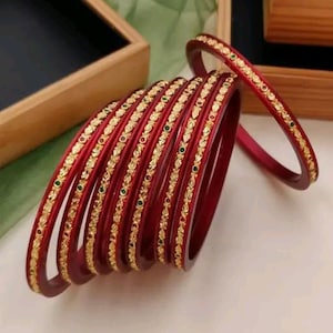 May include: A set of ten red glass bangles with gold and green accents. The bangles are decorated with a floral pattern and have a shiny finish.