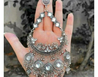 May include: A silver and white ornate earring with a crescent moon design, multiple dangling charms, and mirrored accents.