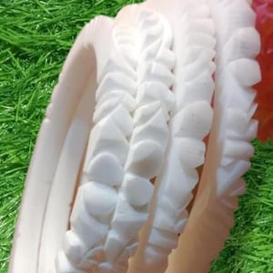 May include: Three white bangles with a decorative, textured design. The bangles are stacked on top of each other and are made of a smooth, white material.