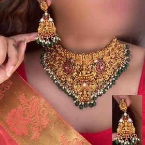 Può includere: Un set di collana e orecchini in oro con disegni intricati che raffigurano divinità e perline verdi. La collana è di tipo choker con un design ampio e decorato. Gli orecchini sono lunghi e pendenti con dettagli simili.