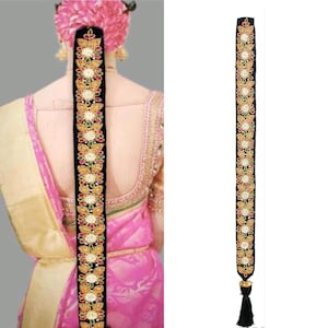 May include: Black velvet hair extension with gold and colorful embellishments. The extension has a tassel at the bottom.