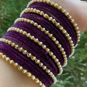 May include: A set of purple velvet bangles with gold trim and white beads.