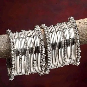 May include: A set of silver bangles with intricate designs. The bangles are stacked on top of each other and have a shiny finish.