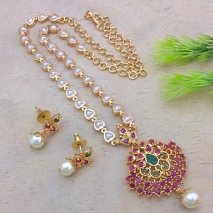 Könnte beinhalten: Eine goldene Halskette mit einem Anhänger aus rosa und grünem Stein und Perlenakzenten. Die Halskette wird mit passenden Ohrringen mit Perlenanhängern geliefert.