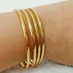 May include: A set of four gold-colored bangles stacked on a person's wrist. The bangles are smooth and shiny.