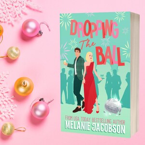 May include: A teal book cover with the title "Dropping the Ball" in white and red letters. The cover features a couple in formal attire, a disco ball, and a party scene. The author's name, "Melanie Jacobson", is printed in white at the bottom of the cover.