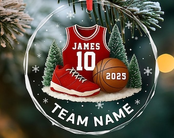 May include: A clear, round Christmas ornament with a red ribbon. Inside, a red basketball jersey with "JAMES 10", a red sneaker, and a basketball with "2025". The words "TEAM NAME" are at the bottom.