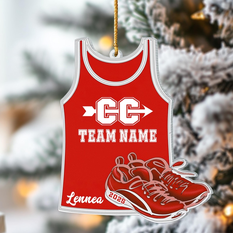 May include: Red and white ornament shaped like a cross country running jersey and shoes. The jersey has the letters "CC" with an arrow, the words "TEAM NAME", and the name "Lennea". The shoes have the year "2025".