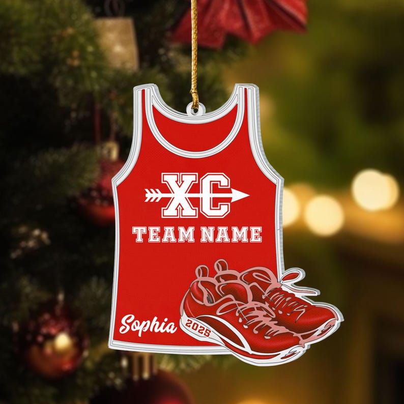 May include: Red and white ornament shaped like a running singlet, with the text "XC TEAM NAME" and a pair of red running shoes. The name "Sophia" and the year "2025" are also visible. The ornament hangs from a gold string.